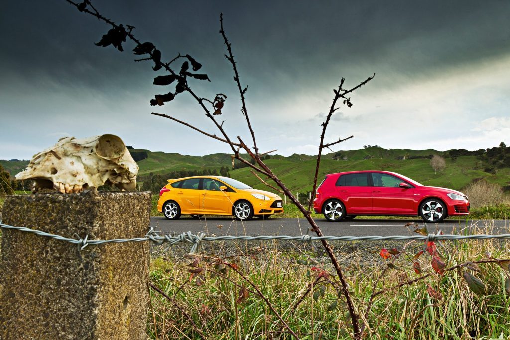 2013 VW Golf GTI vs Ford Focus ST parked on road with sheep skull in foreground