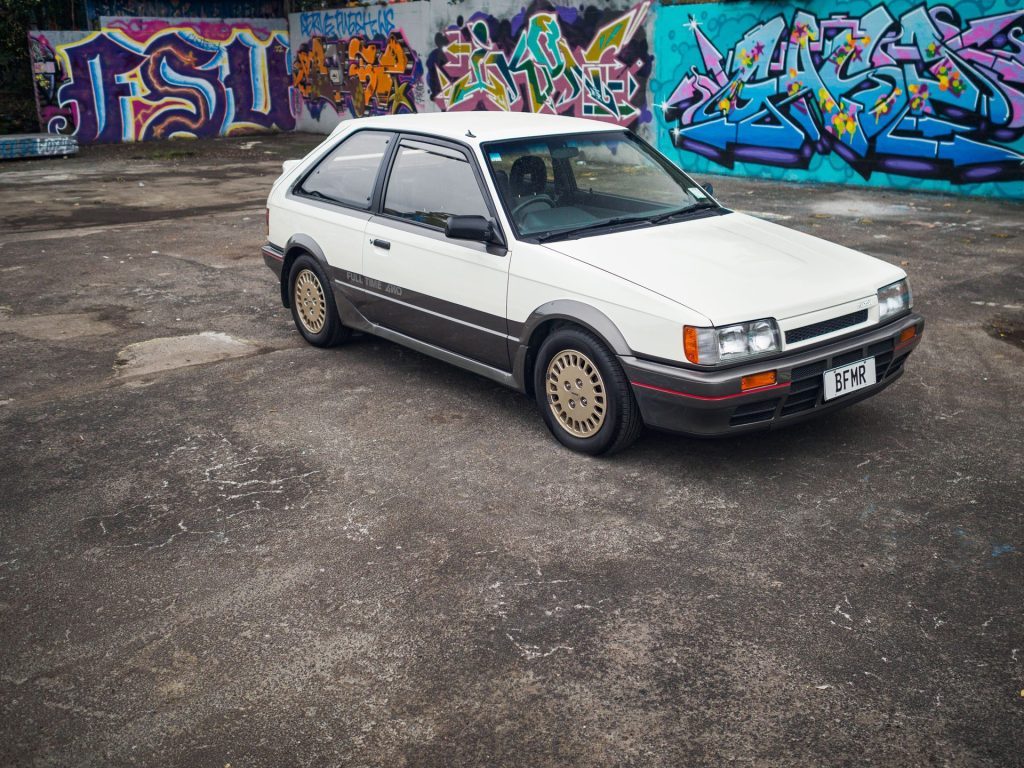 1986 Mazda Familia GT in front of graffiti wall