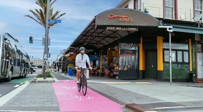 Man riding bike in cycle lane past shops
