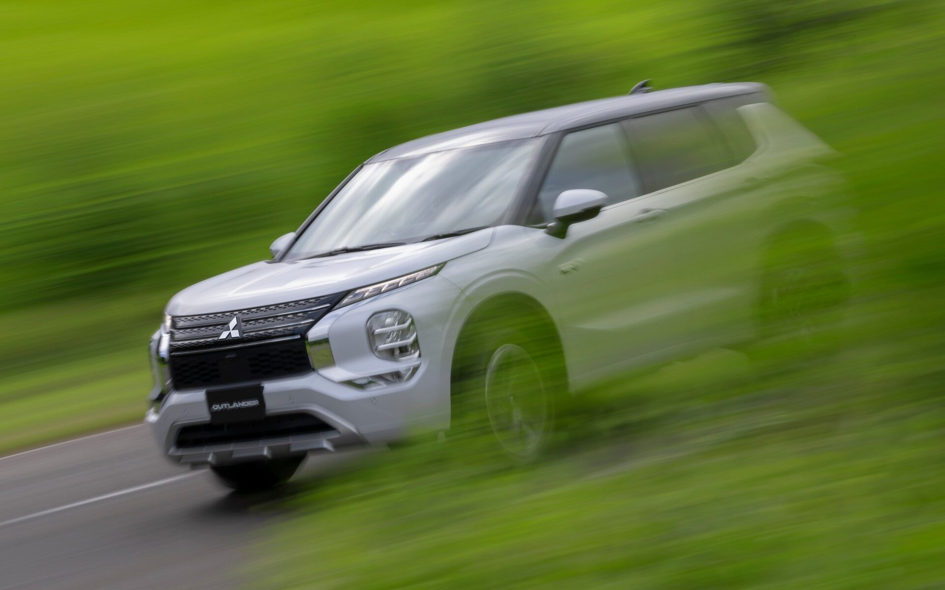 Mitsubishi Outlander PHEV driving past trees front three quarter view