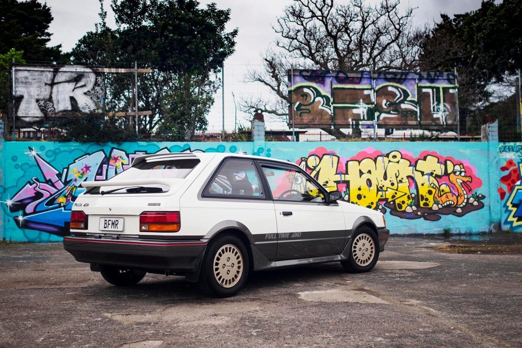 1986 Mazda Familia 4x4 DOHC Turbo parked in front of graffiti