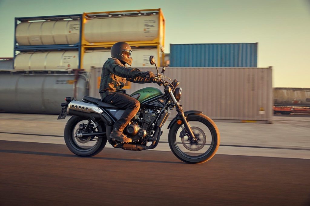 Honda CL500 riding past containers