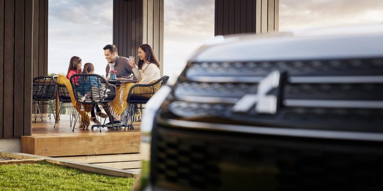 Family sitting at table with Mitsubishi Outlander in foreground