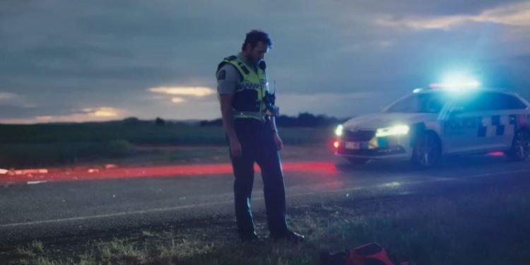 New Zealand police officer actor standing in front of patrol car
