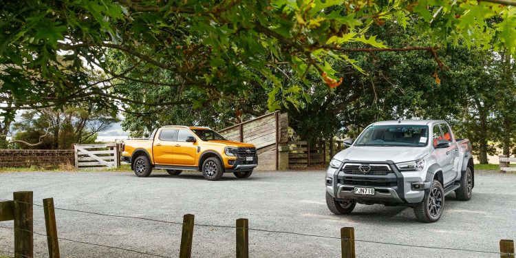 Ford Ranger Wildtrak vs Toyota Hilux SR5 Cruiser front static with fenc ein foreground