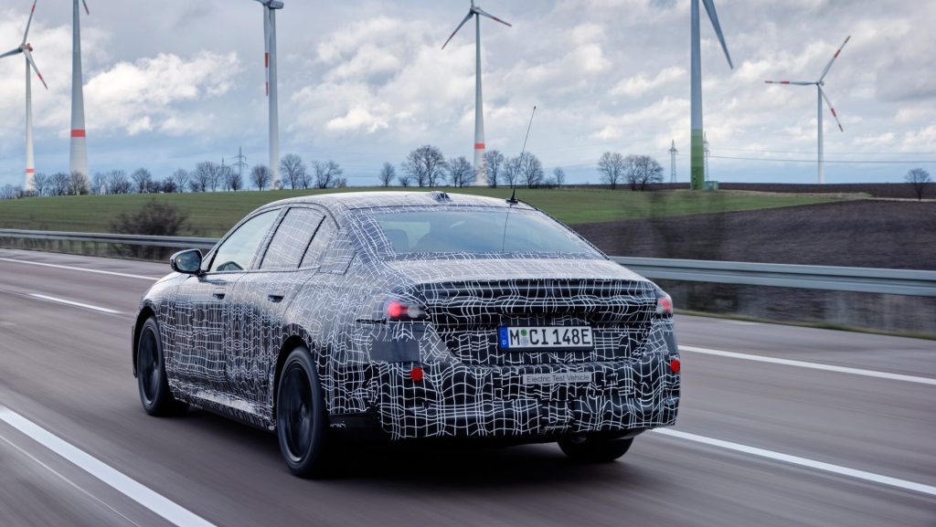 BMW i5 driving on highway next to wind farm