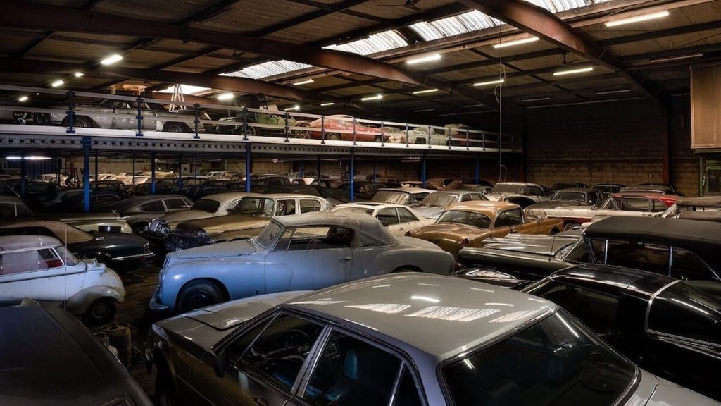 Old cars covered in dust parked in warehouse