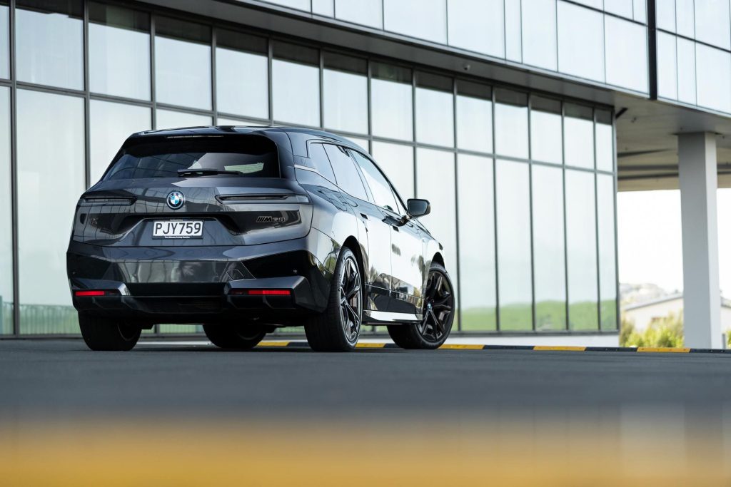 BMW iX M60 rear view parked in front of a glass wall