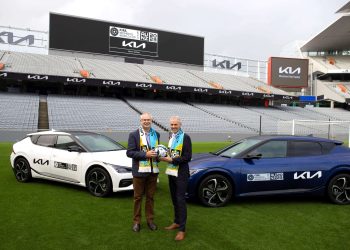 Two mean standing with FIFA Women's World Cup next to electric Kia SUVs