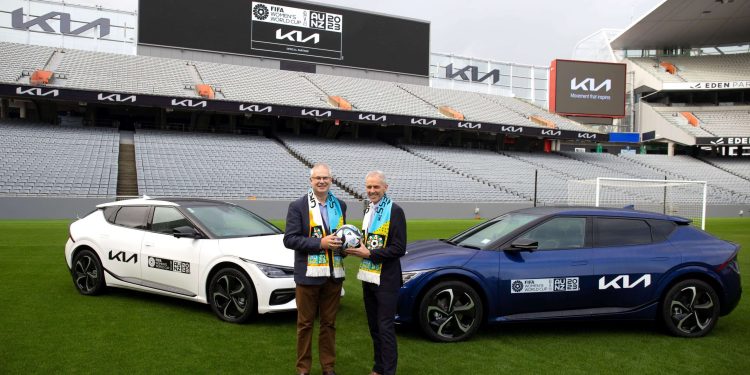 Two mean standing with FIFA Women's World Cup next to electric Kia SUVs