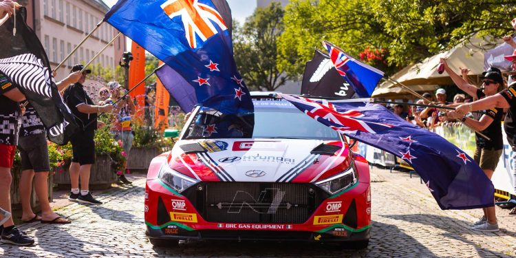 Hayden Paddon driving Hyundai i20 rally car through New Zealand flags