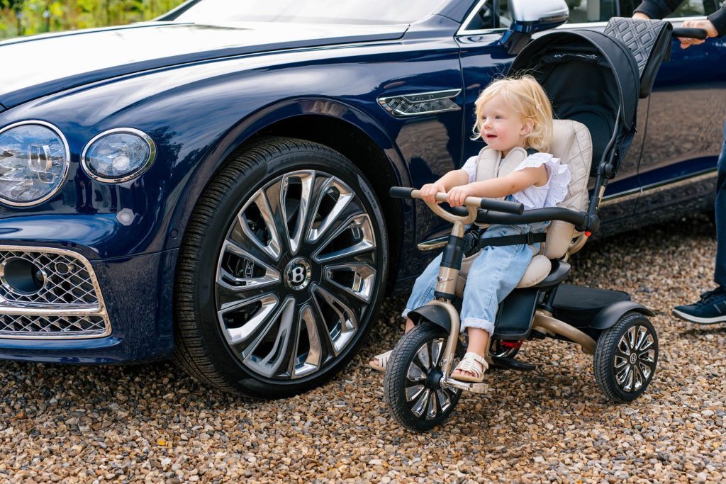 Child sitting on Bentley Mulliner tricycle next to Flying Spur