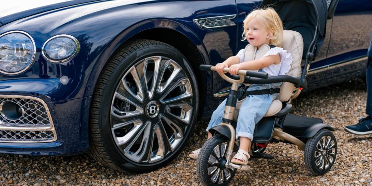 Child sitting on Bentley Mulliner tricycle next to Flying Spur