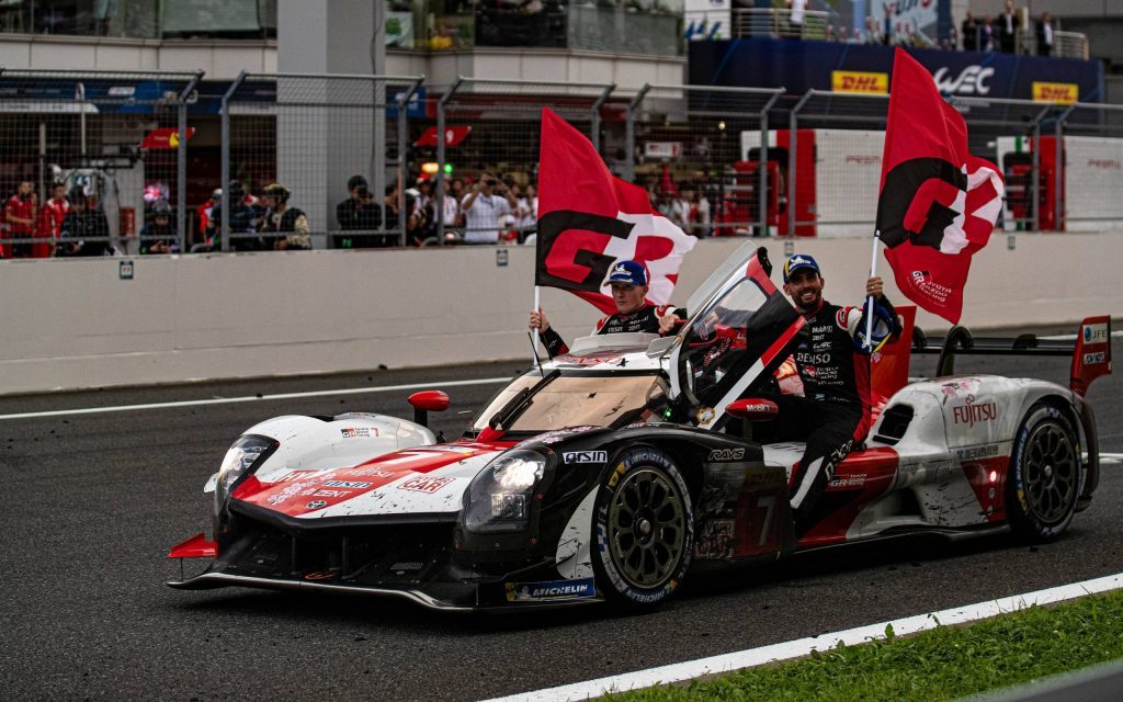 Toyota GR010 with drivers waving flags