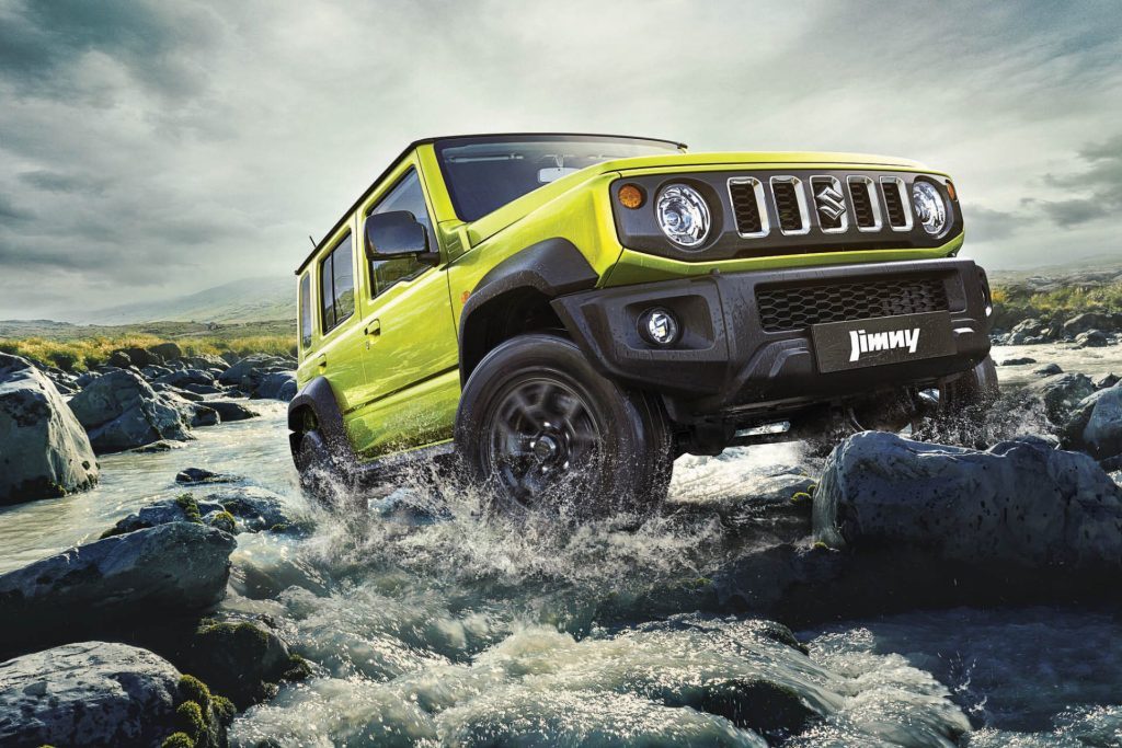 Five-door Suzuki Jimny driving over rocks in river