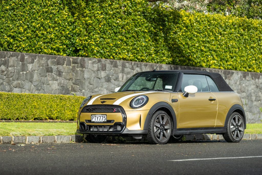Mini Cooper S Convertible in gold, parked next to a large hedge
