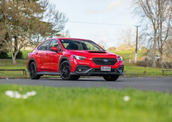 SUbaru WRX AKA in red, parked on tarmac with field behind it