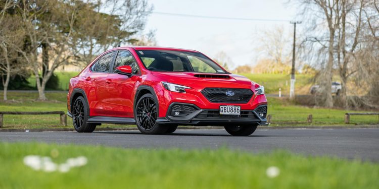 SUbaru WRX AKA in red, parked on tarmac with field behind it