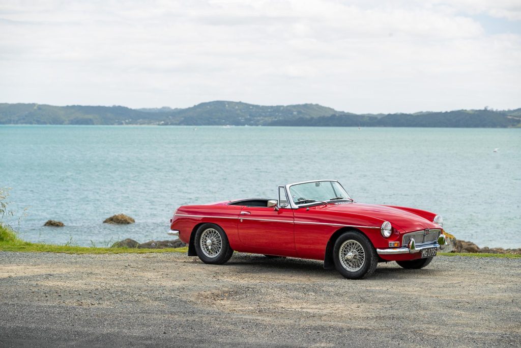 MG MGB Roadster in red, parked on the water's edge, with roof down