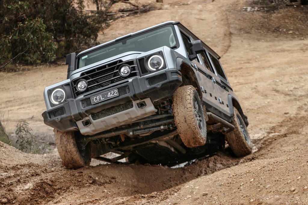 Ineos Grenadier scaling a muddy incline, on three wheels