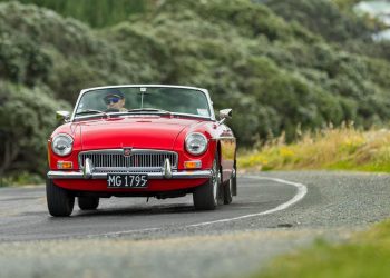 MG MGB Roadster driving around corner by trees