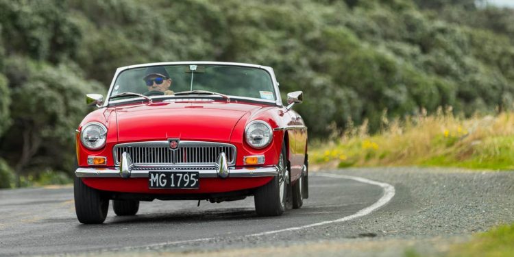 MG MGB Roadster driving around corner by trees