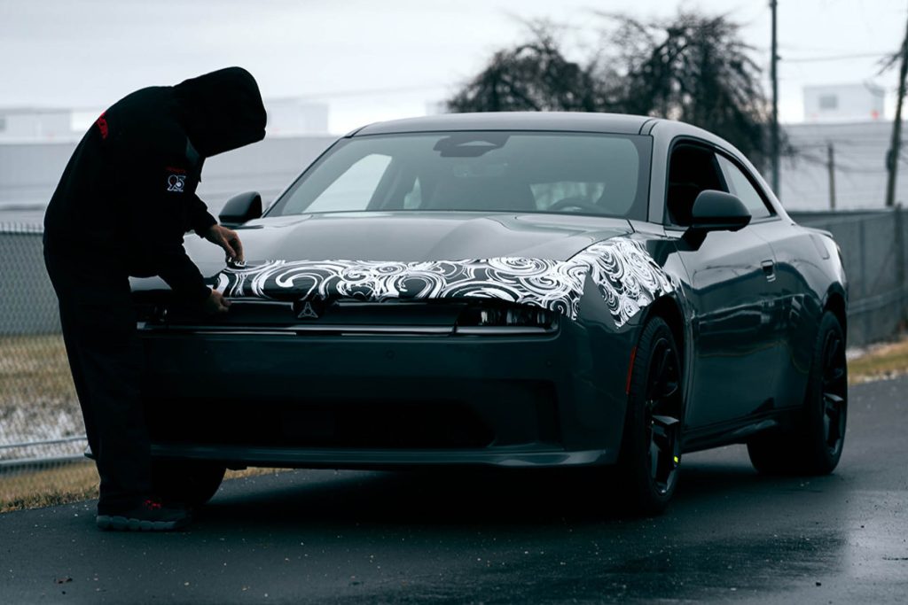 Man removing camouflage from pre-production 2024 Dodge Charger EV
