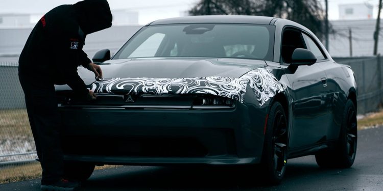 Man removing camouflage from pre-production 2024 Dodge Charger EV