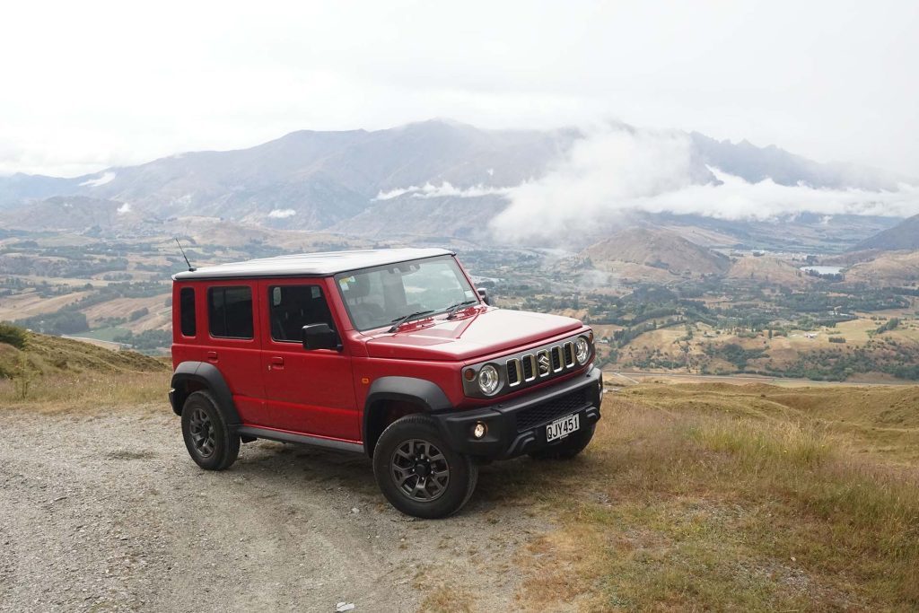 Suzuki Jimny five-door parked on gravel road near mountains