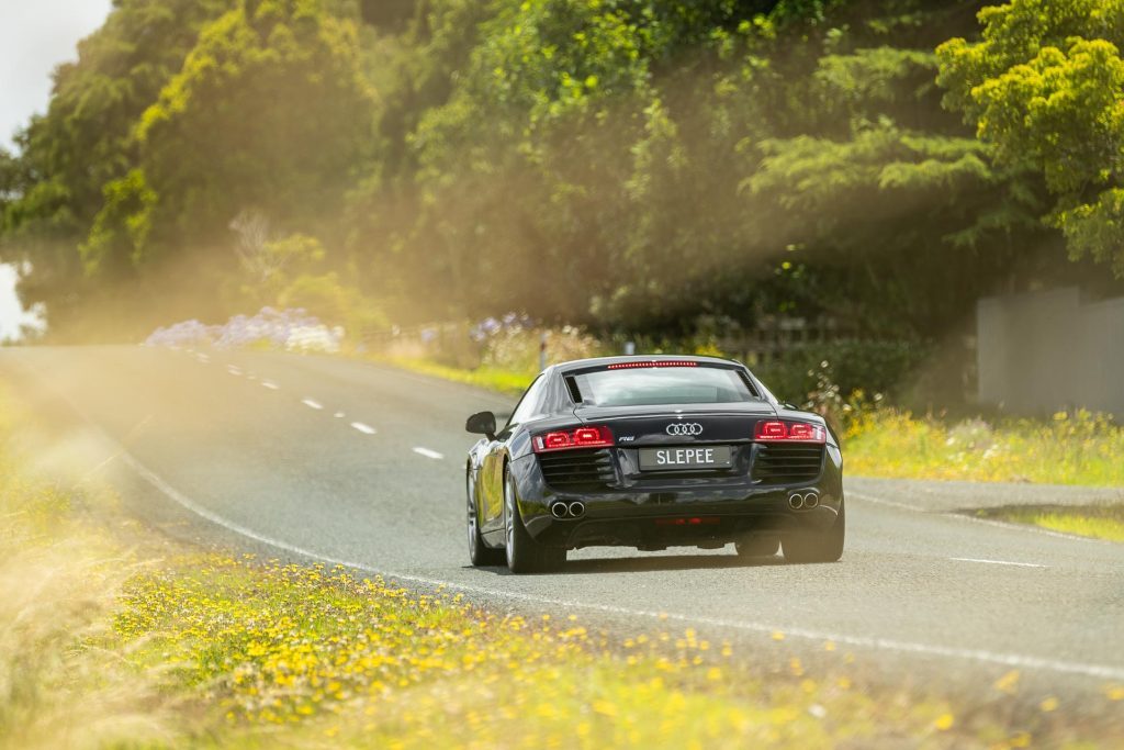Black Audi R8 driving away into the distance, surrounded by flowers