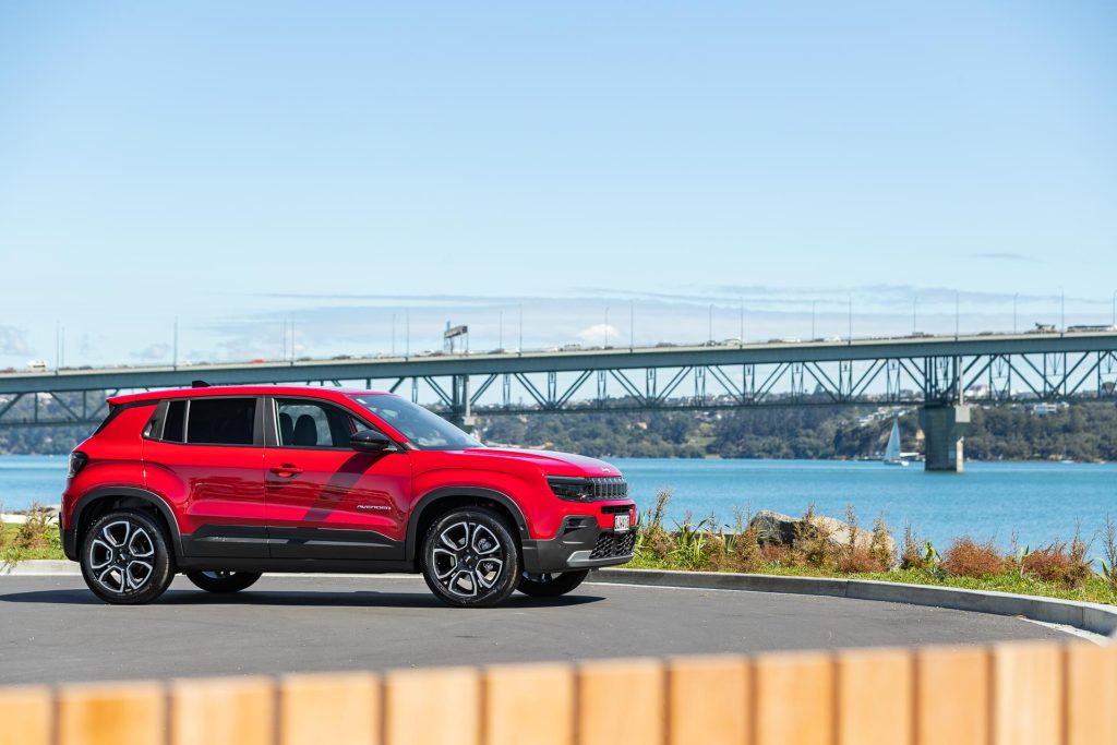 Jeep Avenger in red, parked in front of the Auckland harbour bridge