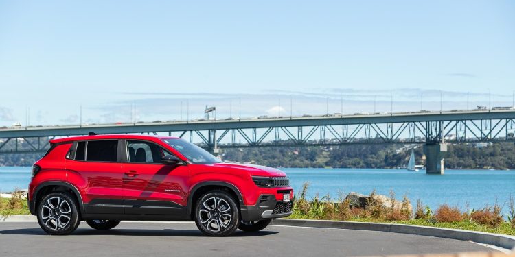 Jeep Avenger in red, parked in front of the Auckland harbour bridge