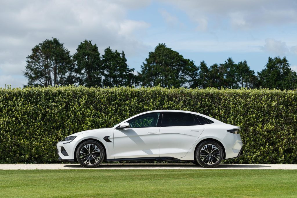 side profile of the BYD Seal Dynamic, pictured in white in front of a hedge