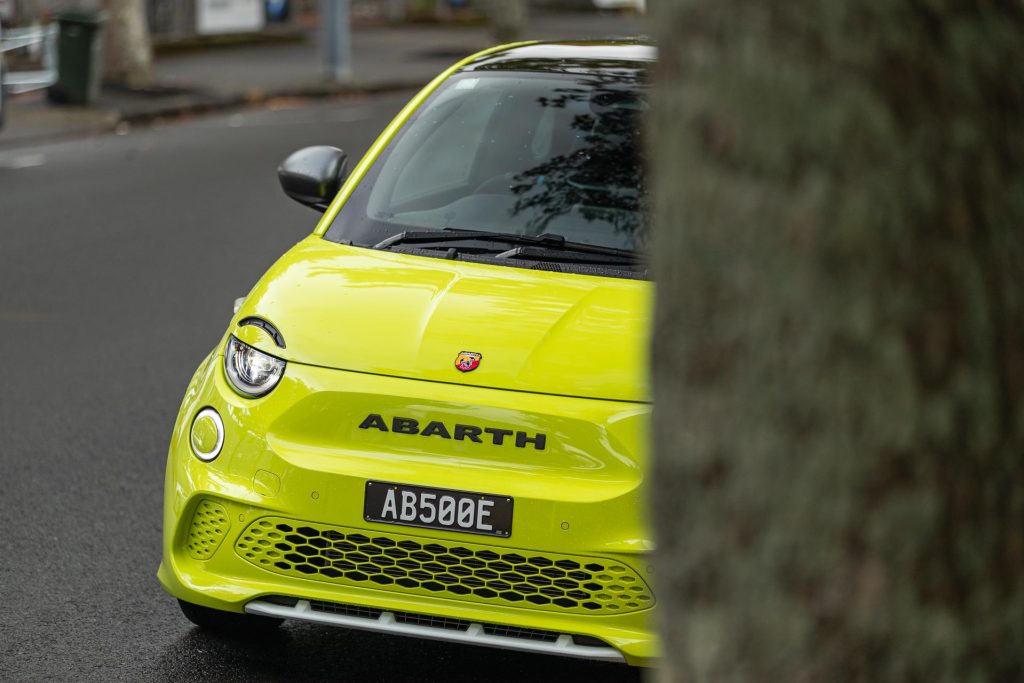 Front of the Abarth 500e Scorpionissima peeping past a tree