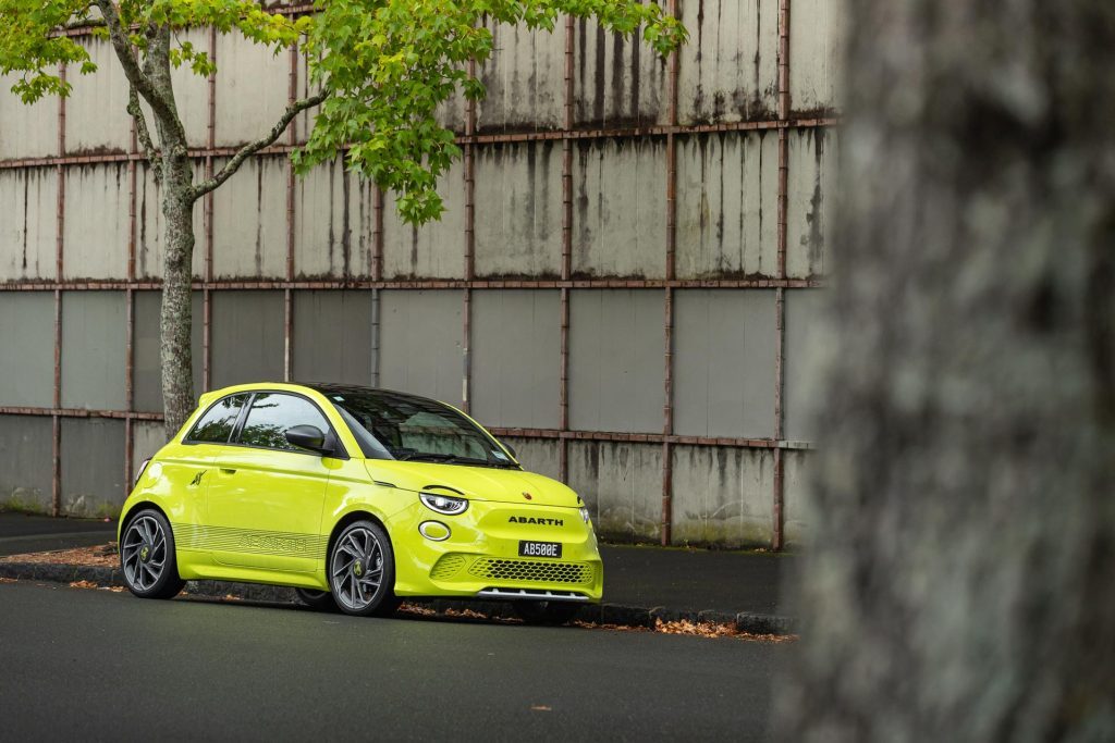 Abarth 500e Scorpionissima front quarter hero shot, parked in front of urban wall