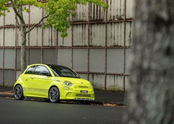 Abarth 500e Scorpionissima front quarter hero shot, parked in front of urban wall