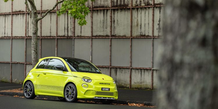 Abarth 500e Scorpionissima front quarter hero shot, parked in front of urban wall