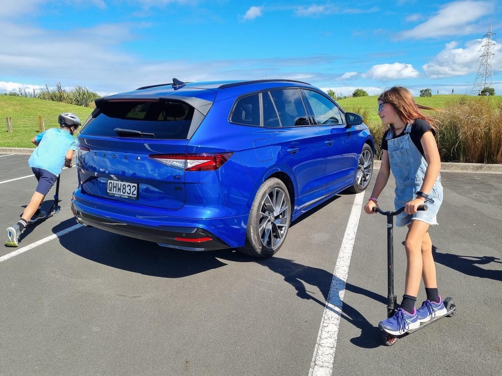 Blue Skoda Enyaq Sportline 80, showing rear quarter as kids scooter around it