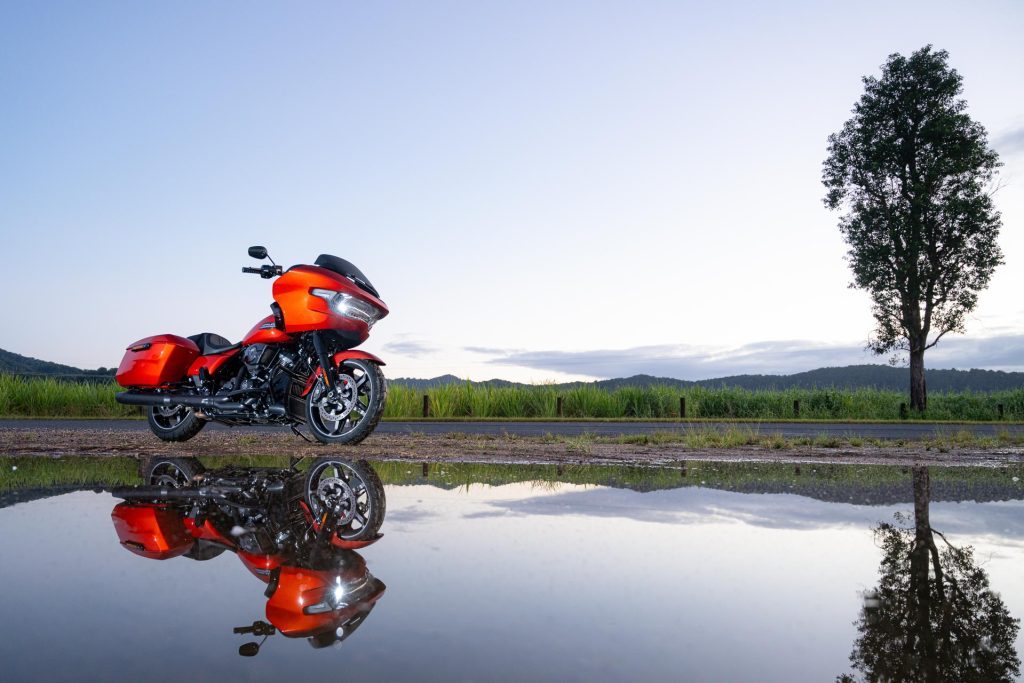 Harley Davidson Road Glide in orange, parked with a reflection below